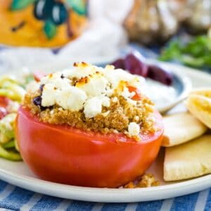 A tomato stuffed with quinoa and topped with feta cheese on a plate with feta cheese.