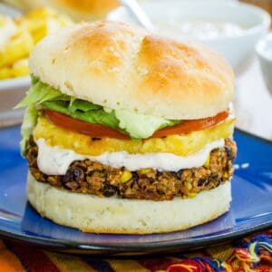 A black bean quinoa burger topped with pineapple and a creamy sauce on a bun on a blue plate.