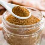 A measuring spoon holds pumpkin pie spice above a jar of spice mix.