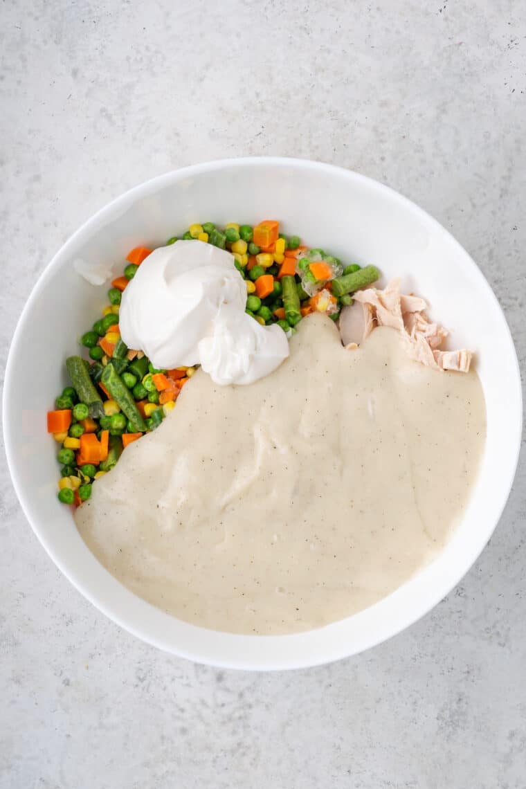 Adding cream soup to the chicken and vegetables in a bowl.
