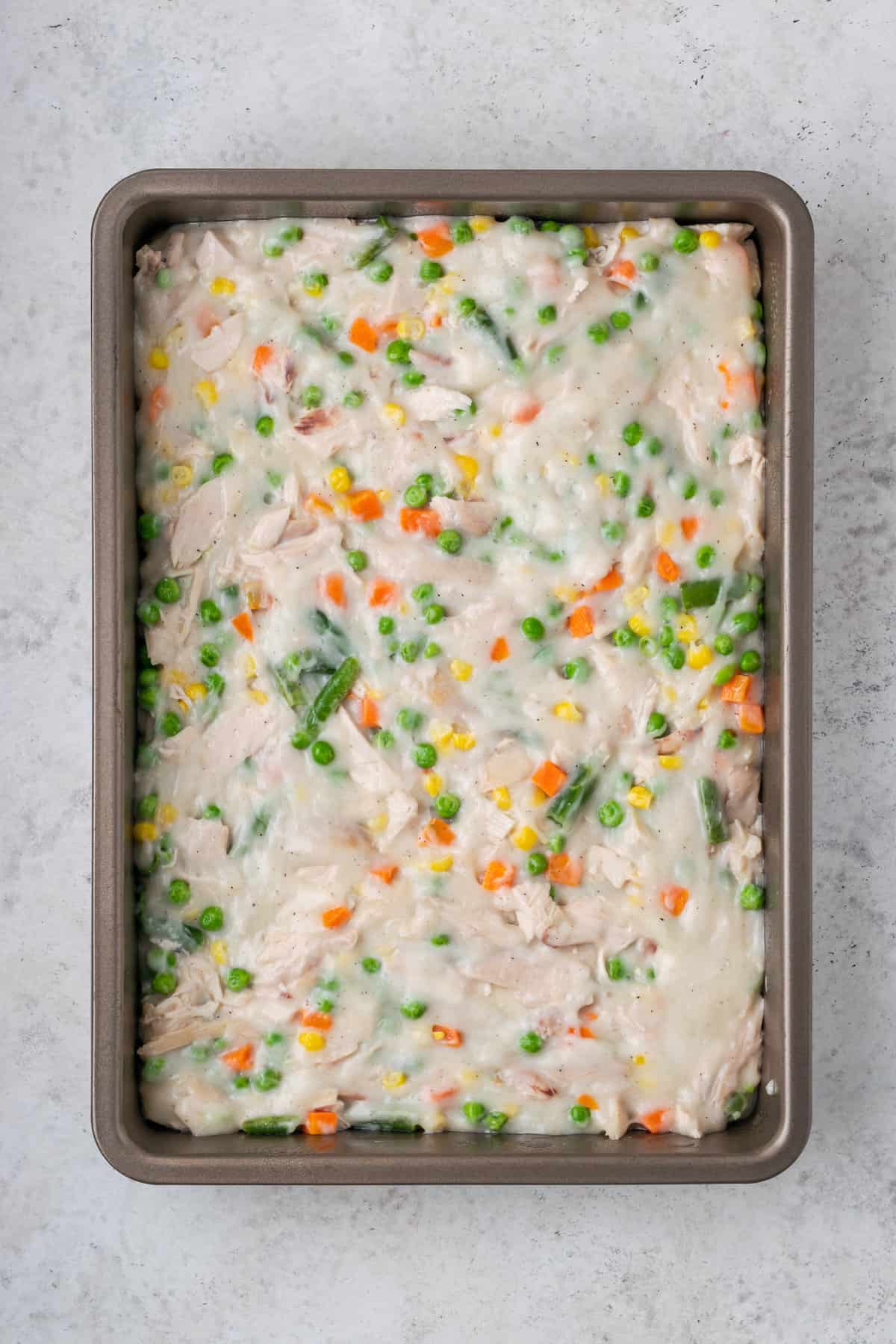 A layer of cream soup and vegetables is seen in a baking dish.