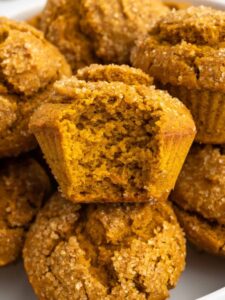 Gluten-free pumpkin muffins on a plate, one has a bite taken out from it.