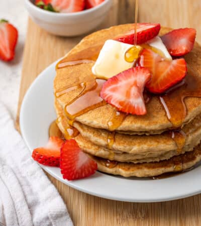 A stack of oatmeal pancakes on a white plate topped with strawberries.