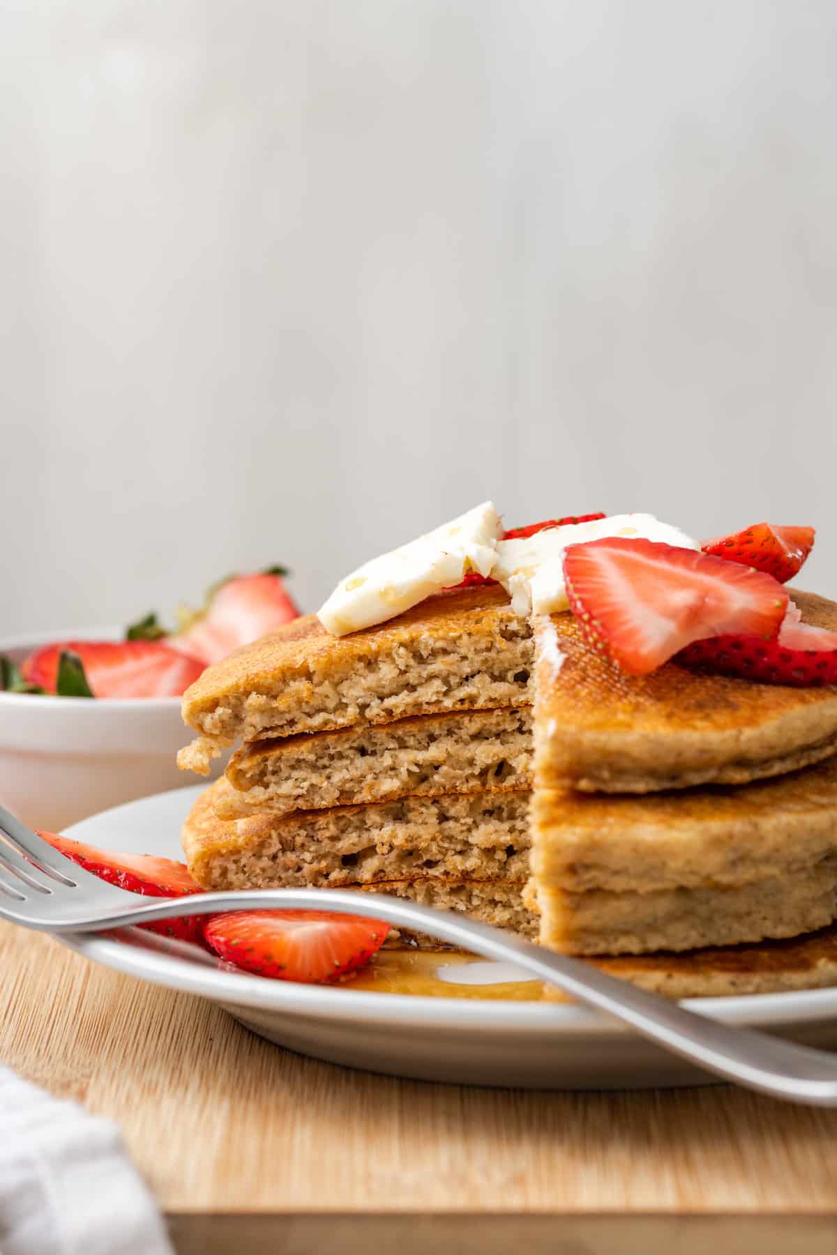 A stack of oatmeal pancakes on a white plate topped with strawberries.