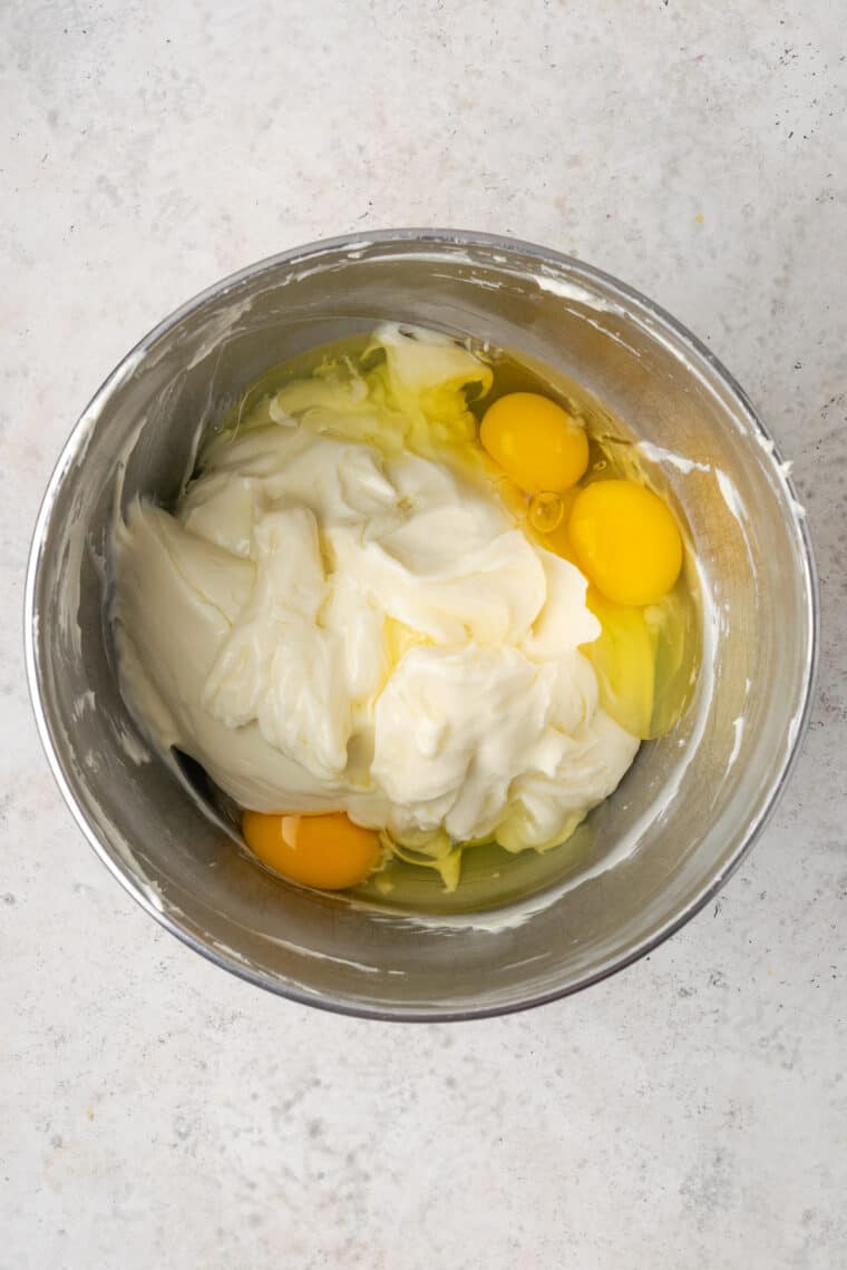 Adding eggs to cream cheese filling in a metal bowl.