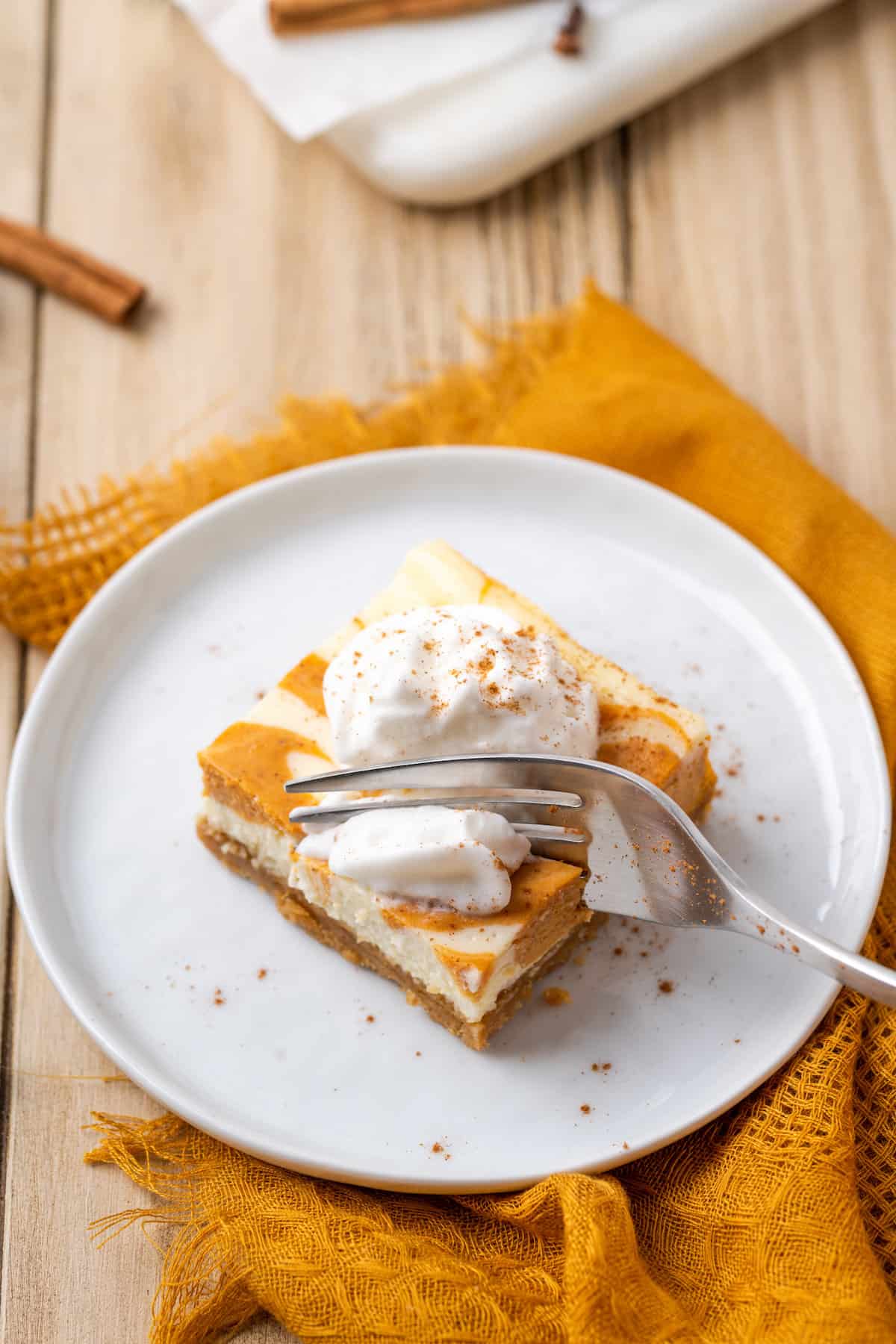 A fork cuts into a pumpkin cream cheese bar on a plate.