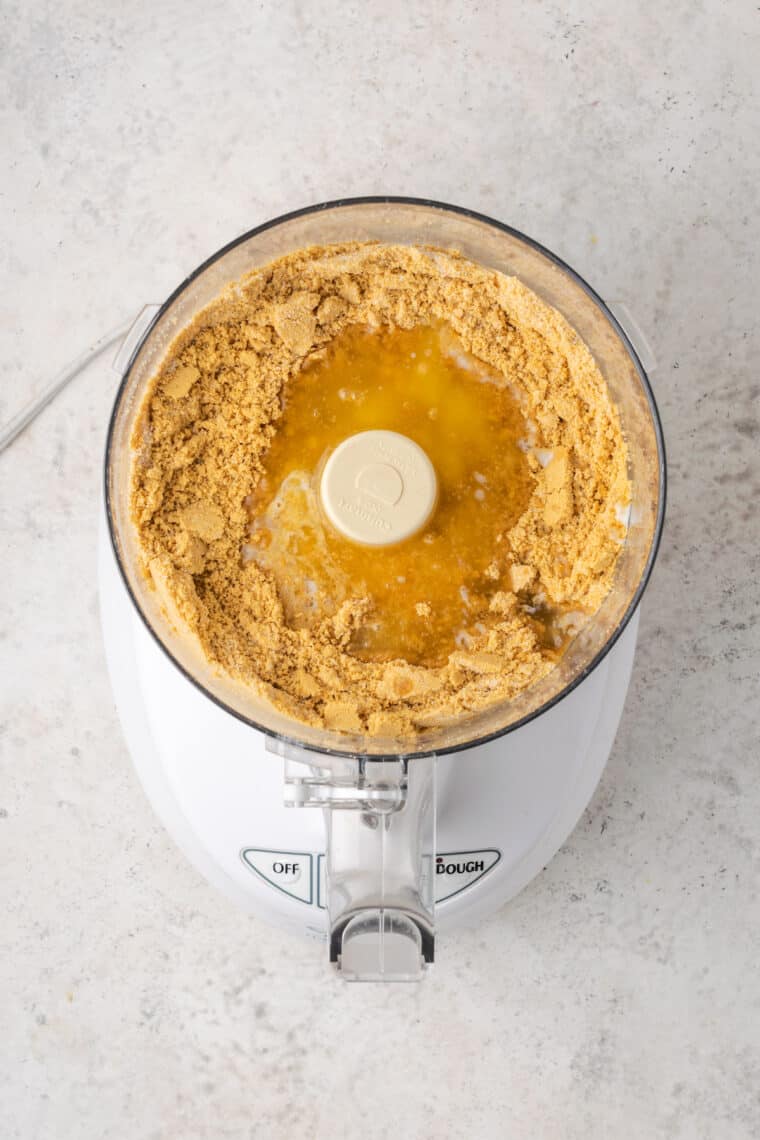 A graham cracker crust with butter in a food processor.