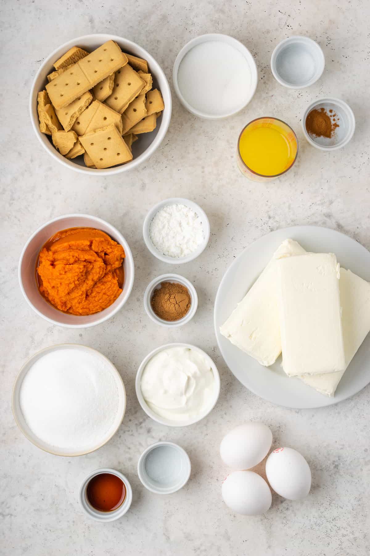 Ingredients for pumpkin cheesecake bars: cream cheese, butter, pumpkin, graham crackers, eggs, sour cream, sugar.