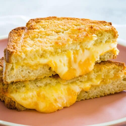 Two triangular halves of a grilled cheese sandwich on top of each other with cheese oozing out.