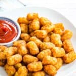 A white plate full of air fryer tater tots and ketchup.