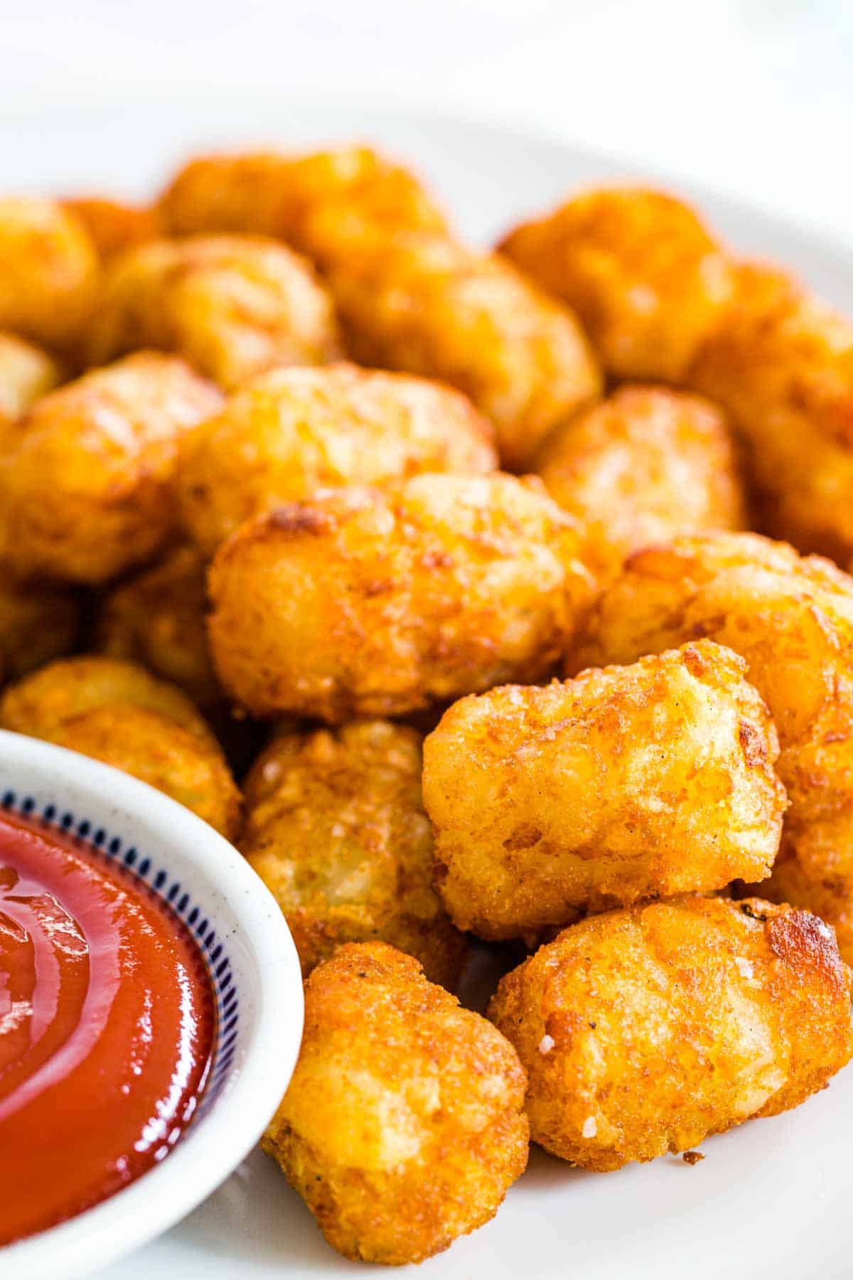 A white plate full of air fryer tater tots and ketchup.
