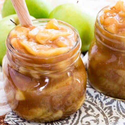 A glass jar of apple pie filling with a wooden spoon in it.