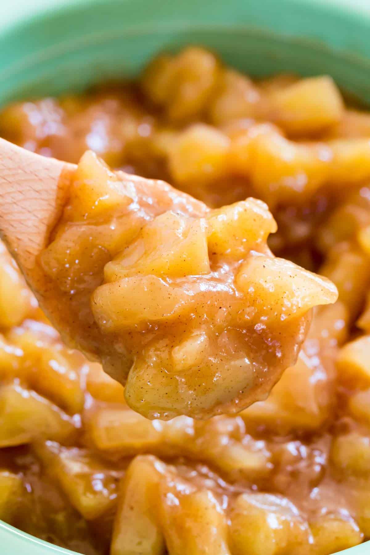 A close up of apple pie filling with a wooden spoon.