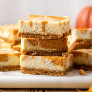 Three swirled pumpkin cheesecake bars stacked on each other with more scattered in the background.