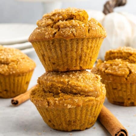 Two stacked pumpkin muffins with more in the background.