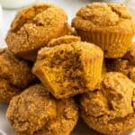 A pile of pumpkin muffins on a white plate with a bite out of the one in the middle with text overlay that says "Gluten Free Pumpkin Muffins".