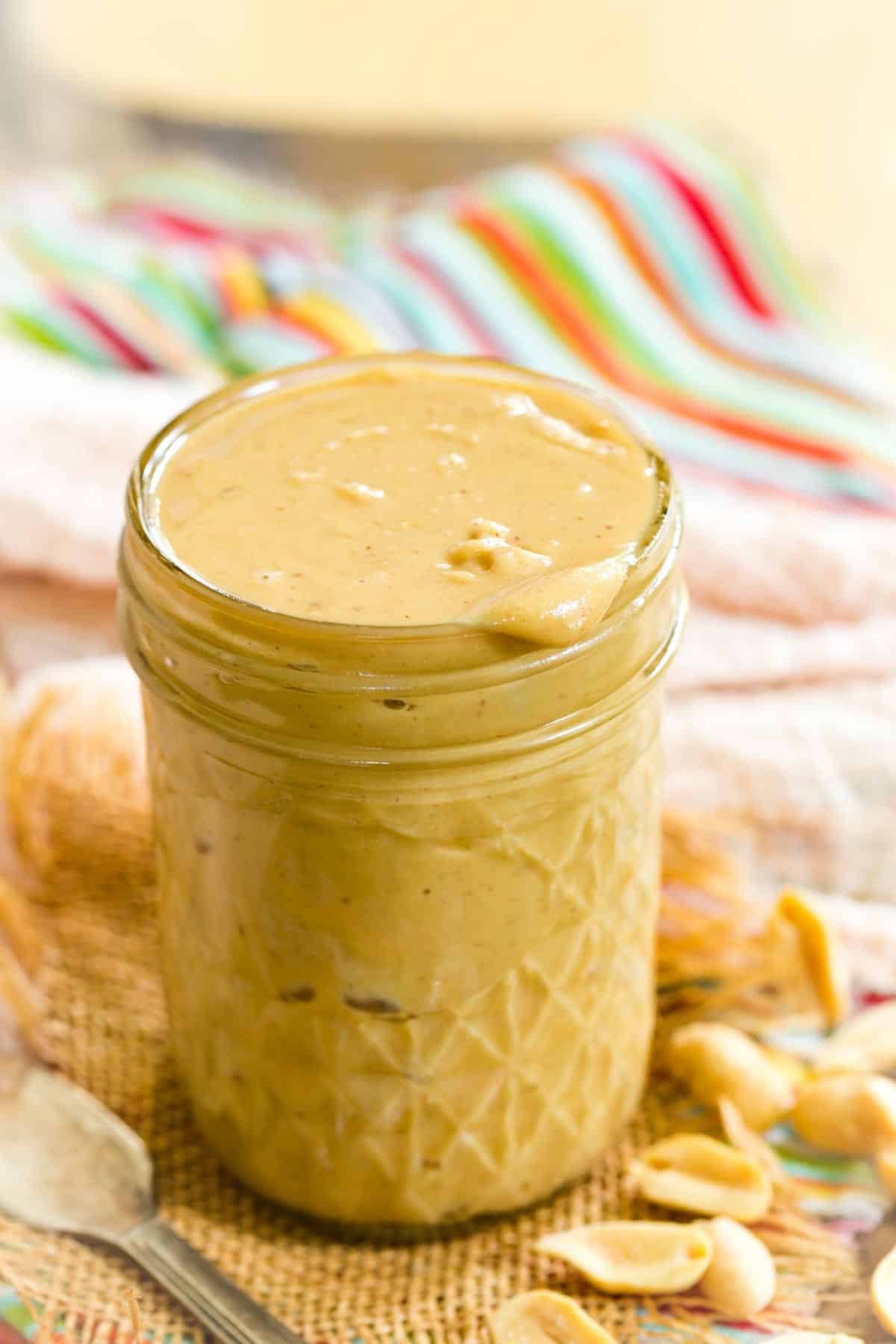 A jar of homemade peanut butter is shown with colorful towels in the background.