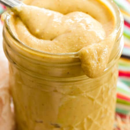 A spoon is shown dipping into a glass jar of homemade peanut butter.