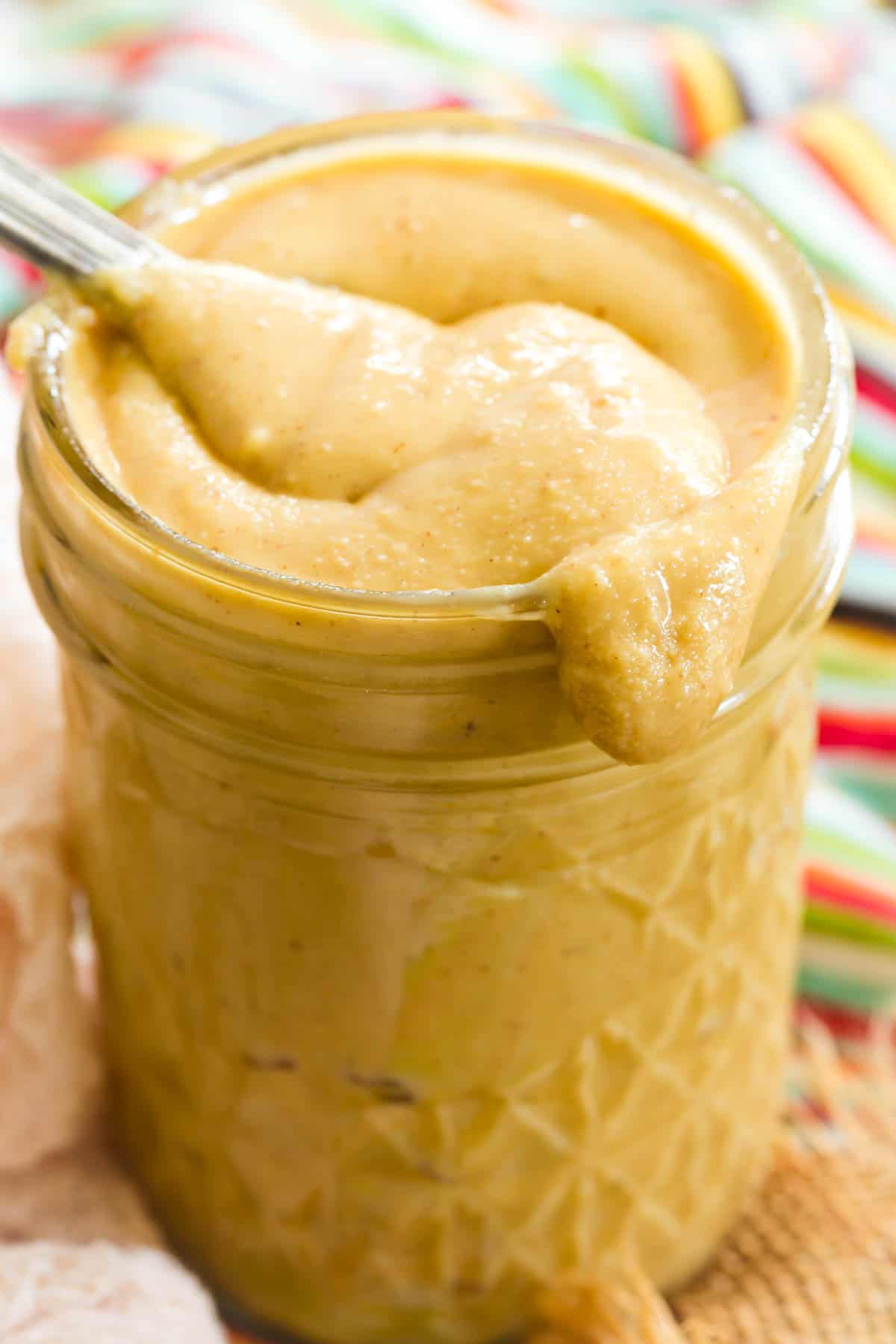 A spoon is shown dipping into a glass jar of homemade peanut butter.