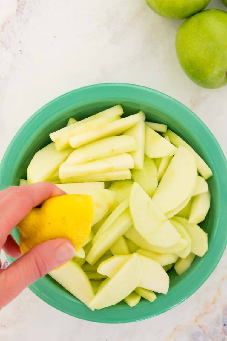 A hand squeezes lemon over sliced apples.