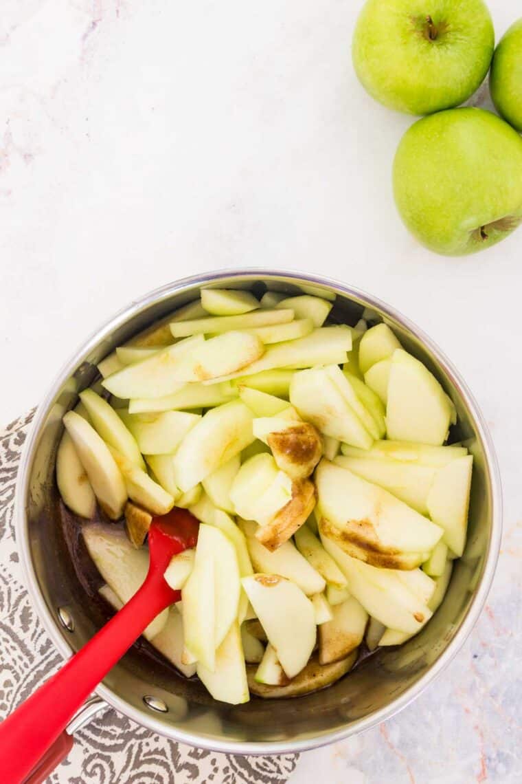 A red spoon stirs apple slices in a bowl.