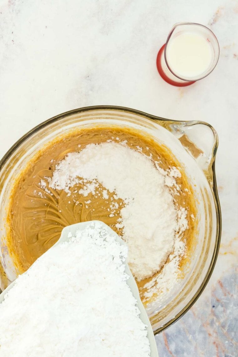 Adding powdered sugar to a bowl of peanut butter frosting.
