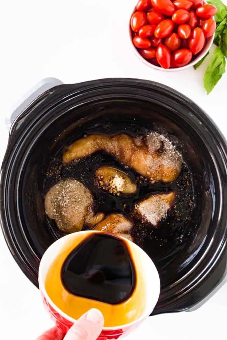 Balsamic vinegar being poured into the crockpot with the seasoned chicken.