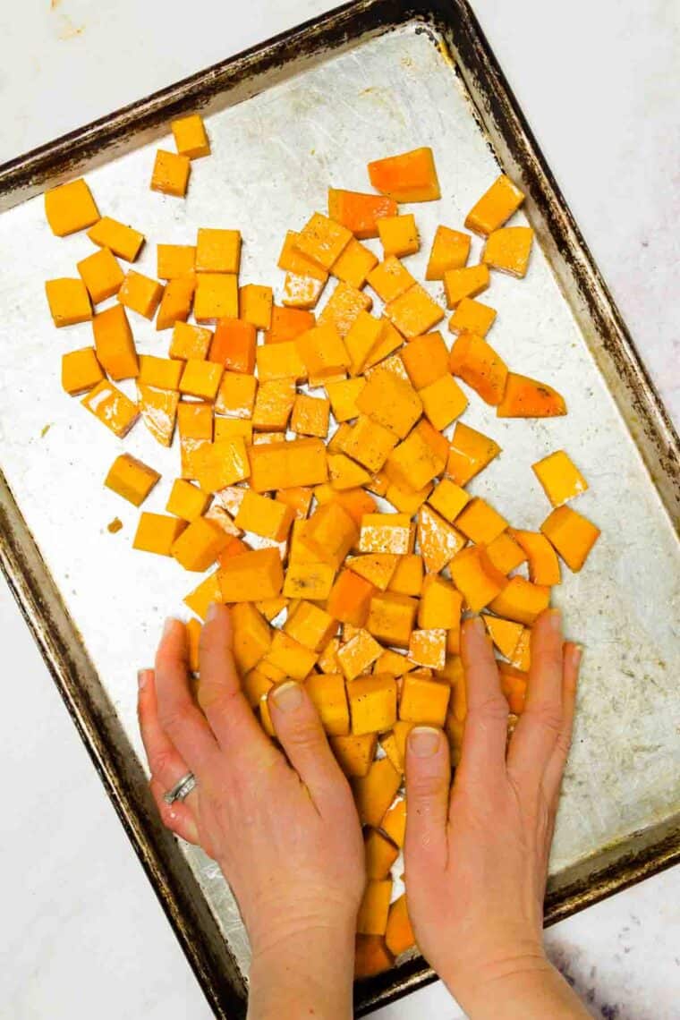 Hands arrange butternut squash cubes on a baking sheet.