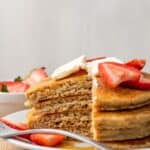 A stack of four pancakes with berries and syrup on top and a wedge cut out of them with text overlay that says "Gluten Free Oatmeal Pancakes".