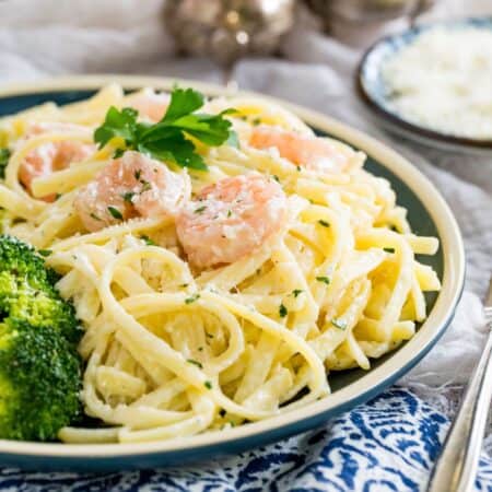 A plate of shrimp alfredo with a sprig of parsley on top and some broccoli on the side.