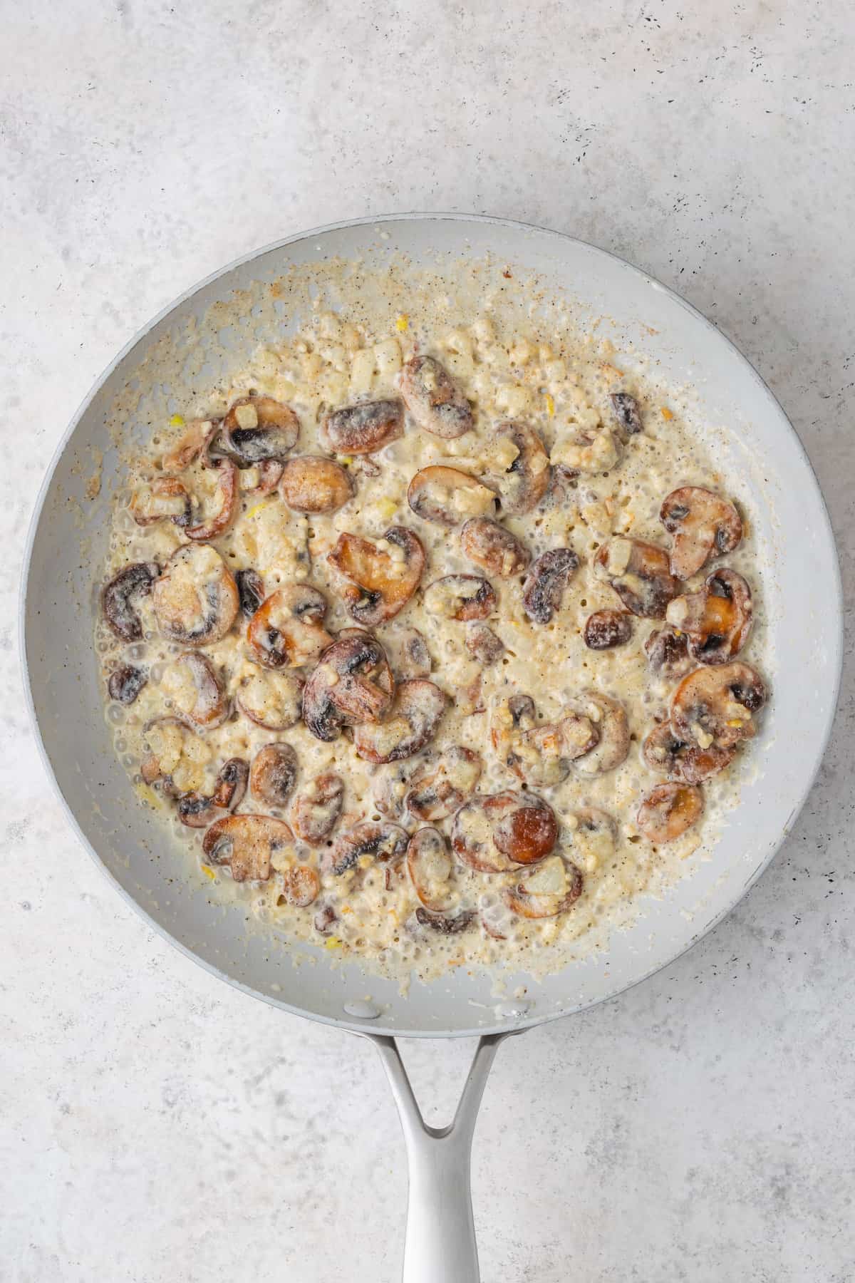 Cooked mushrooms in a skillet with a thickening sauce.