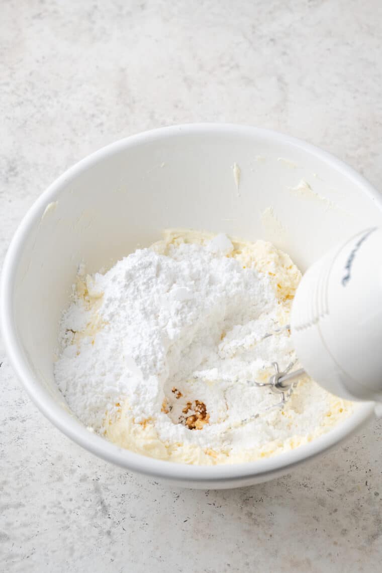 Beating cream cheese and butter together with a hand mixer.