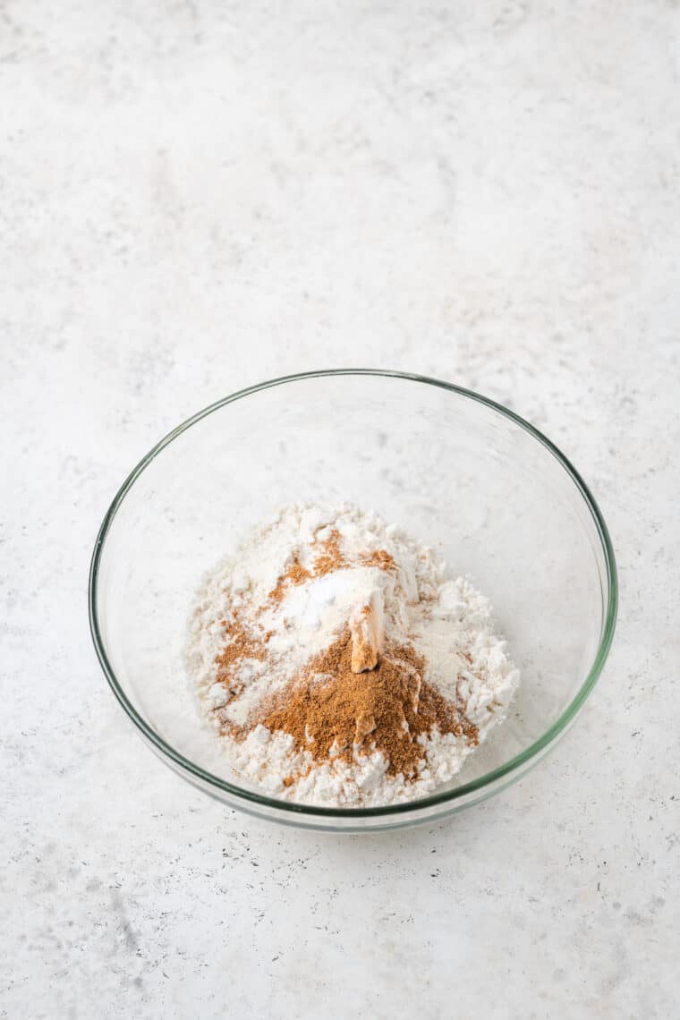 This Gluten-Free Pumpkin Roll takes a tender cake and stuffs it with tangy cream cheese frosting for a gorgeous fall dessert. Dry ingredients for pumpkin roll in a glass bowl.