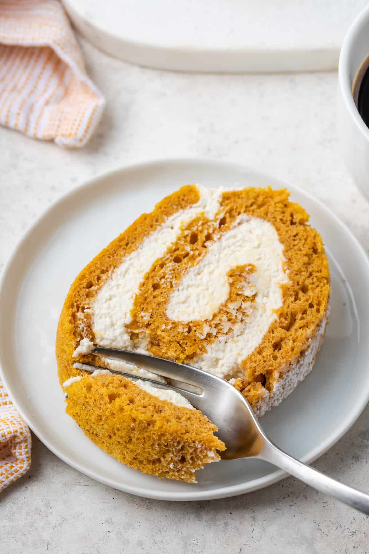A fork cuts into a slice of glute free pumpkin roll on a white plate.