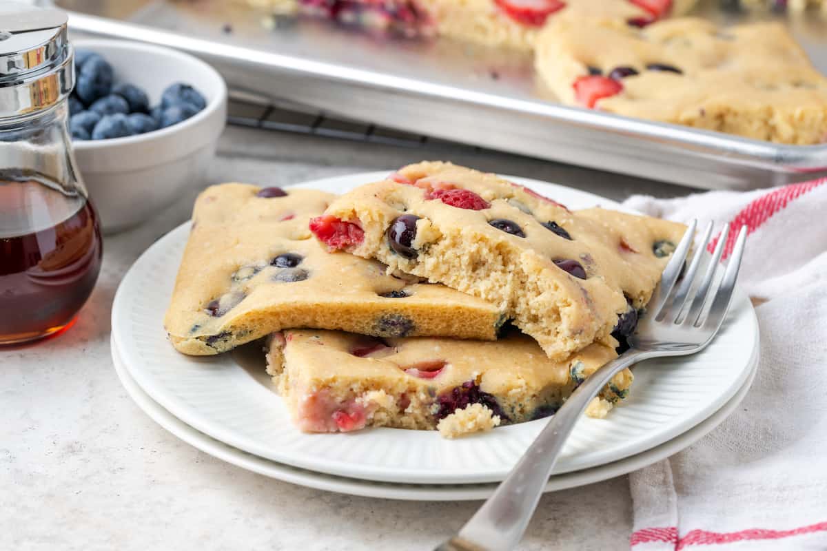 A plate of berry sheet pan pancakes is shown on a white plate with a fork.