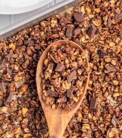 A wooden spoon holds chocolate granola over a pan.