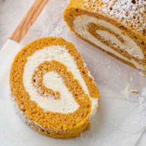 A slice of pumpkin roll cake with a creamy filling on parchment paper.