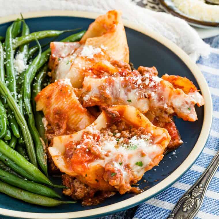 A plate of a serving of stuffed shells with green beans.