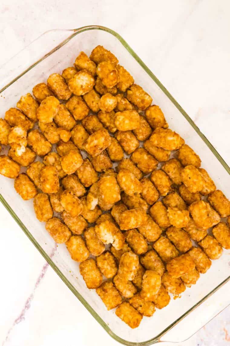 Tater tots are spread into the bottom of a glass baking dish.