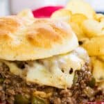 A sloppy joe sandwich with melted cheese on a red and white plate with text overlay that says "Philly Cheesesteak Sloppy Joes".