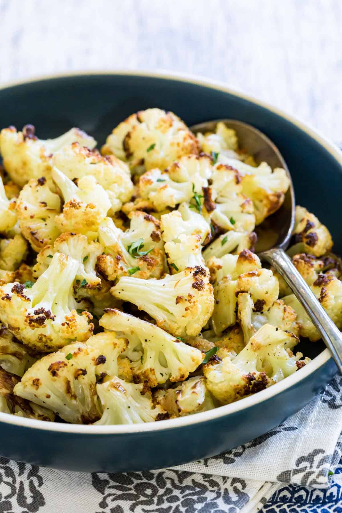 A bowl of roasted cauliflower with a spoon.