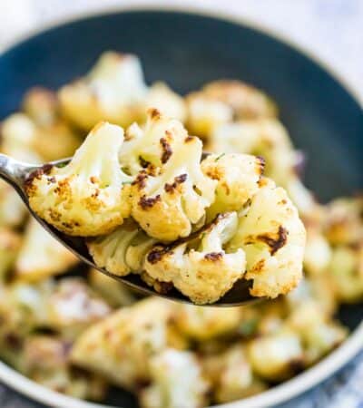 A spoon lifts out roasted cauliflower florets from a bowl.
