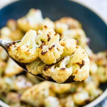 A spoon lifts out roasted cauliflower florets from a bowl.