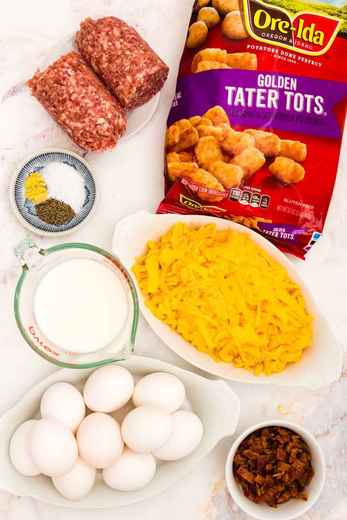 Ingredients for tater tot breakfast casserole are shown including shredded cheese, frozen tater tots, spices, eggs, sausage, and bacon.
