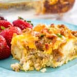 A piece of tater tot breakfast casserole is shown on a blue plate with fresh strawberries.