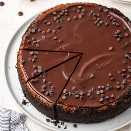 Chocolate cheesecake is shown topped with ganache and chocolate chips.