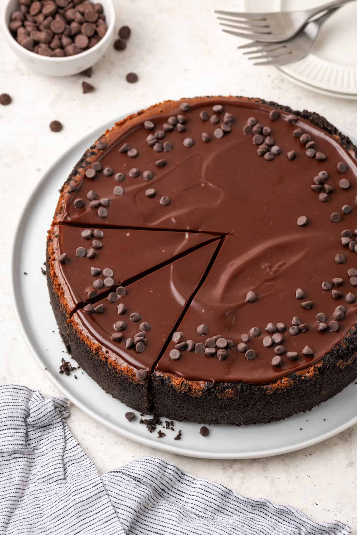 Chocolate cheesecake is shown topped with ganache and chocolate chips.