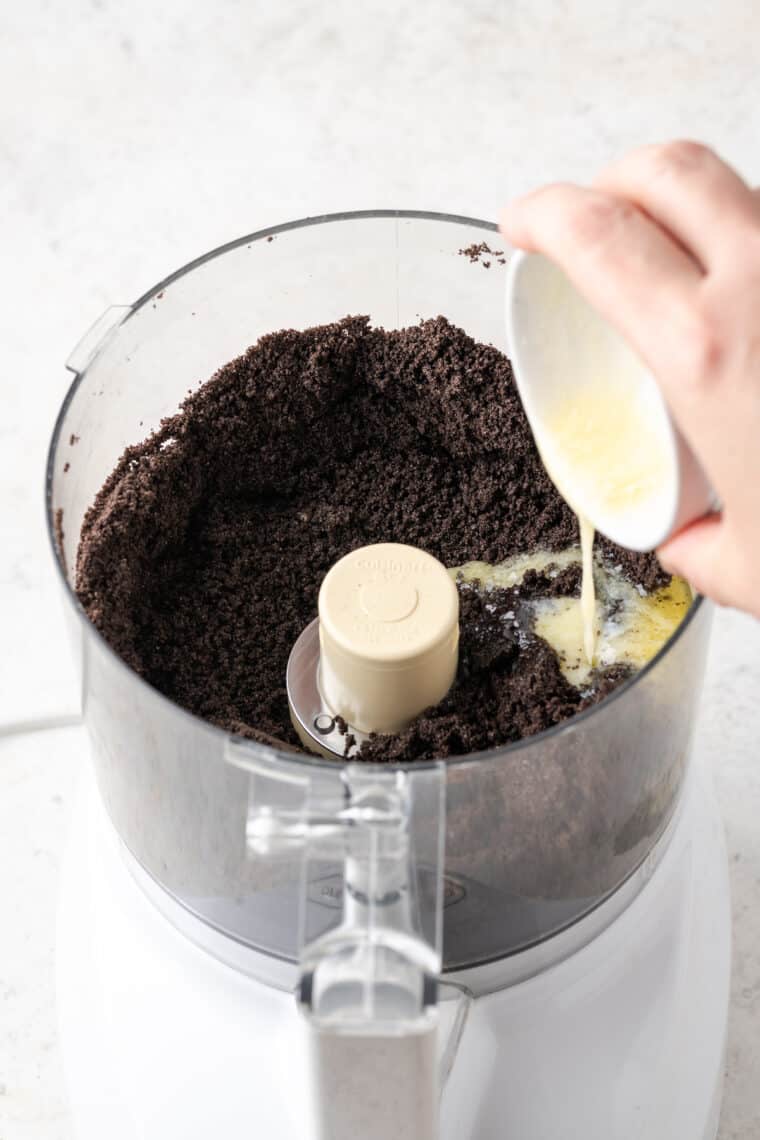 Melted butter is poured into crushed Oreos in a food processor.
