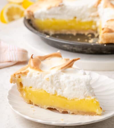 A slice of gluten free lemon meringue pie on a white plate with the pie in the background.