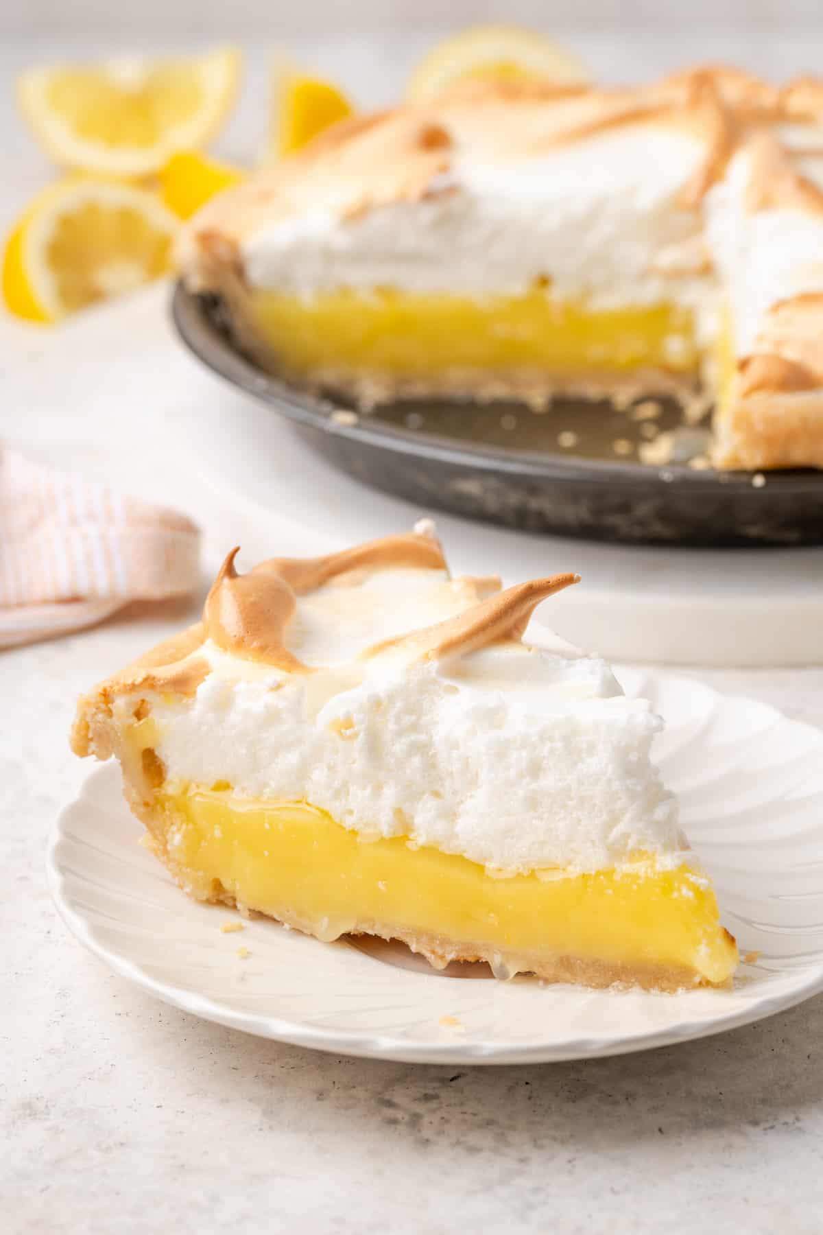 A slice of gluten free lemon meringue pie on a white plate with the pie in the background.
